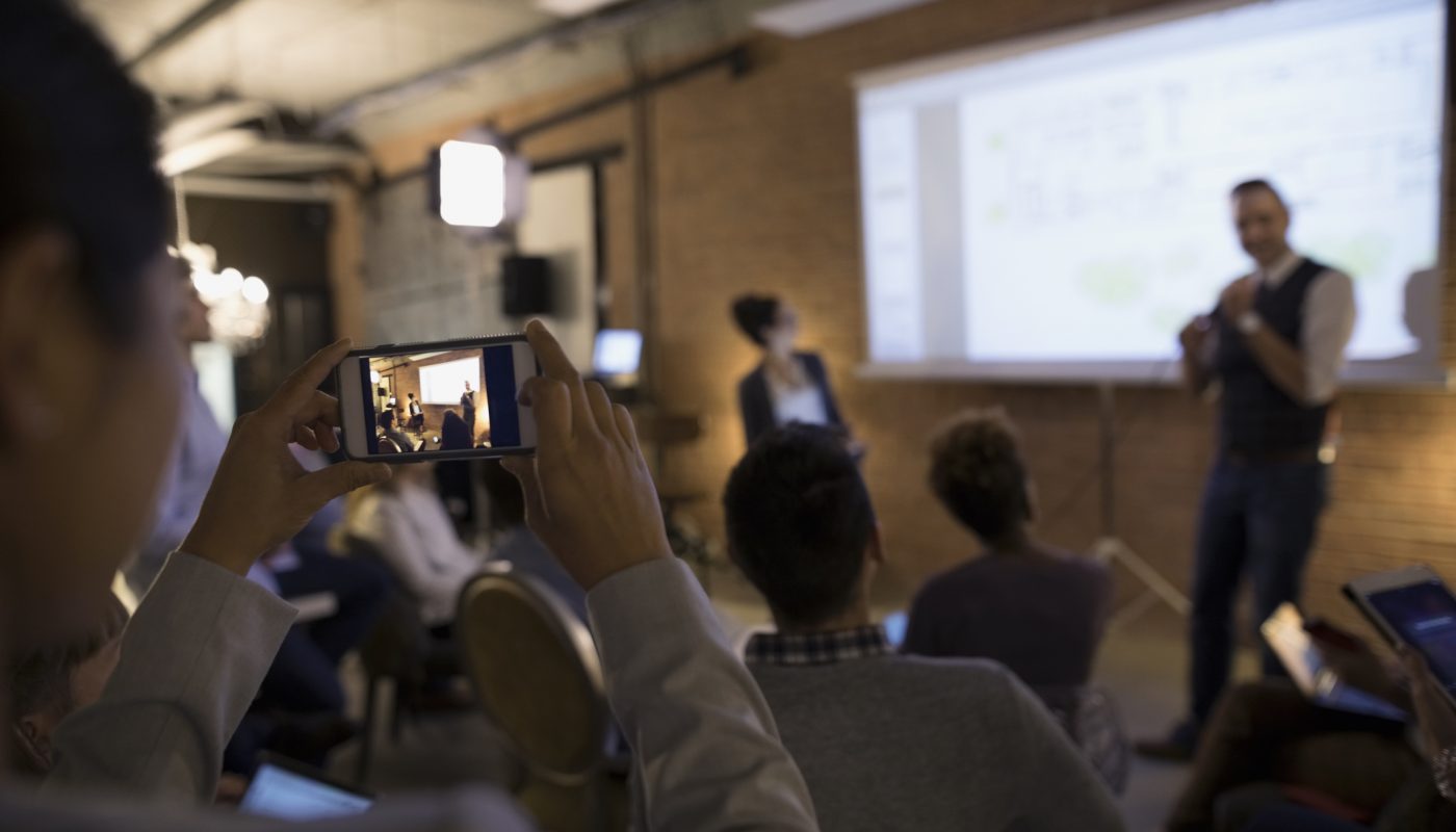 Businesswoman with camera phone videoing conference speaker in conference room